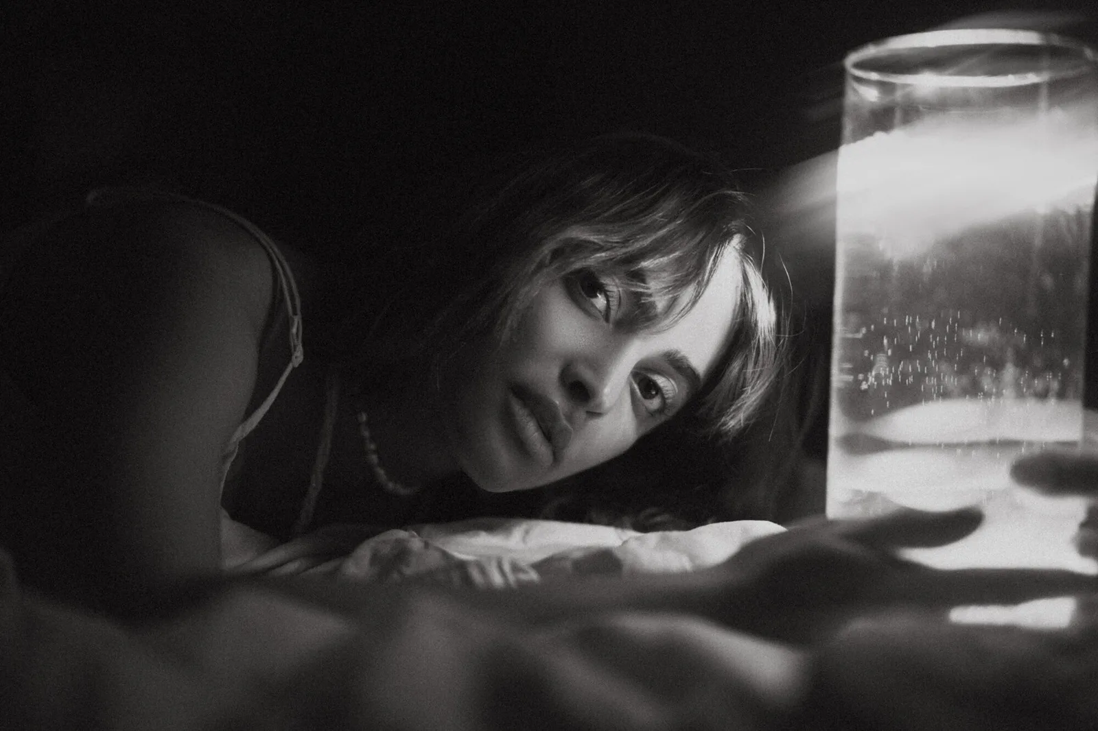 Portrait en noir et blanc d’une femme allongée près d’un verre