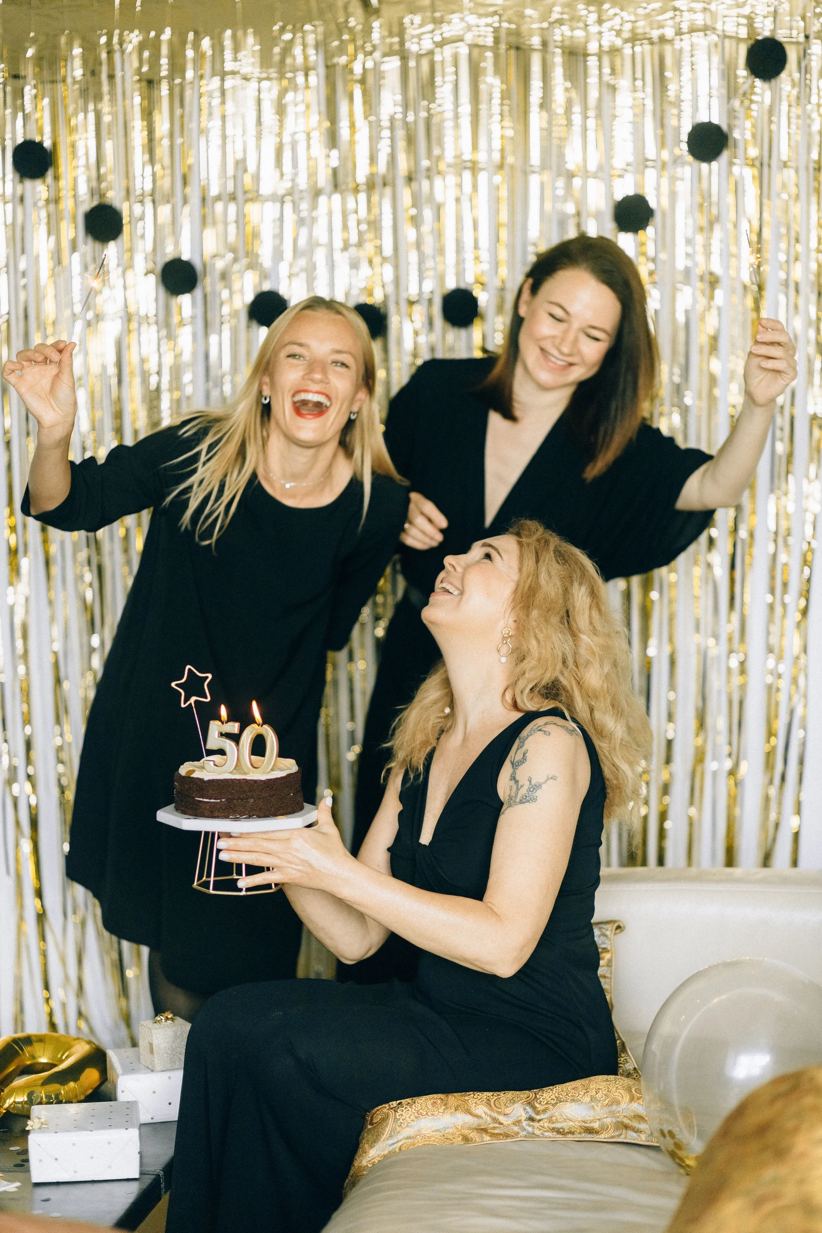 Trois amies fêtent un anniversaire devant un rideau doré