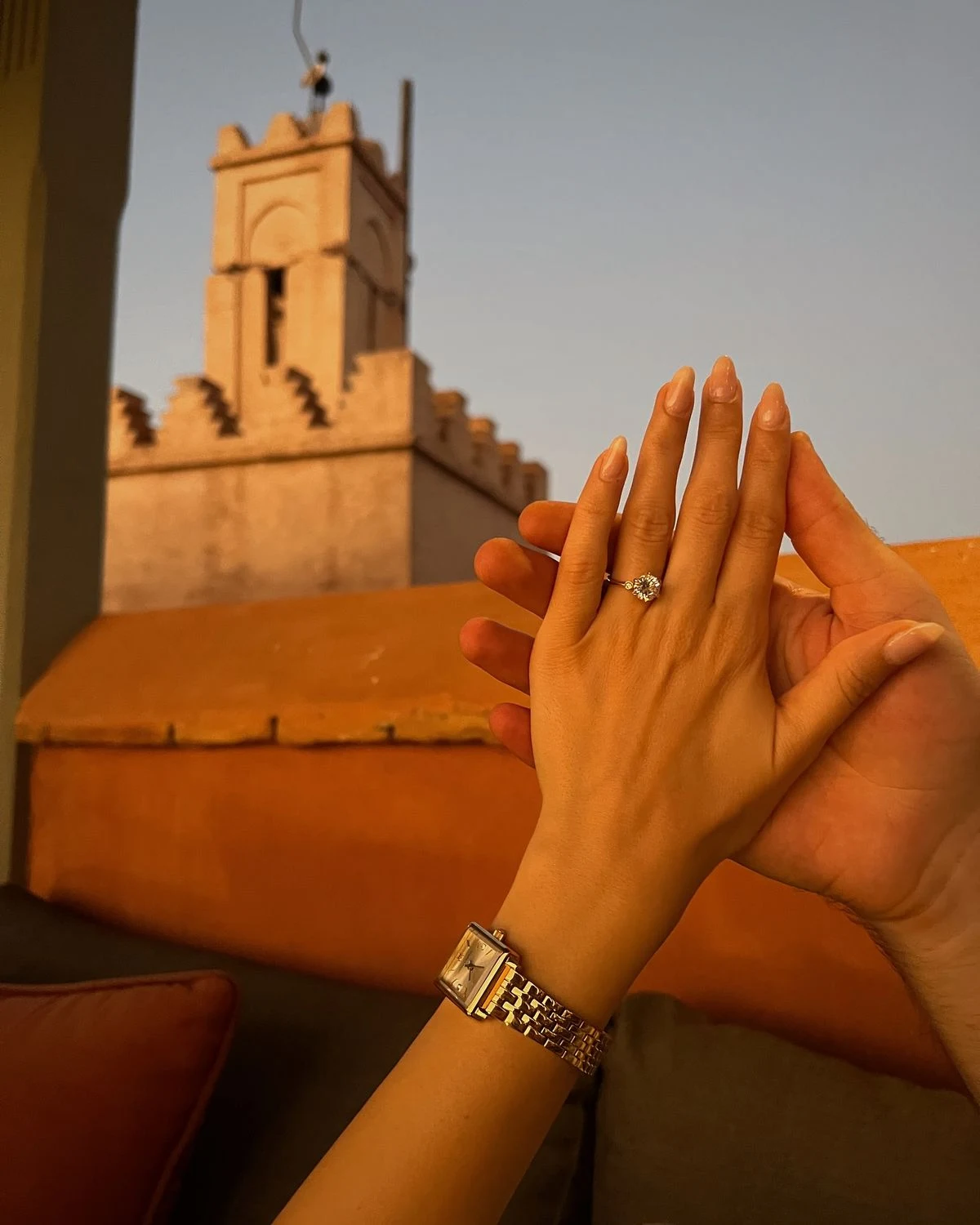 Mains du couple et bague de fiançailles devant une tour en terre