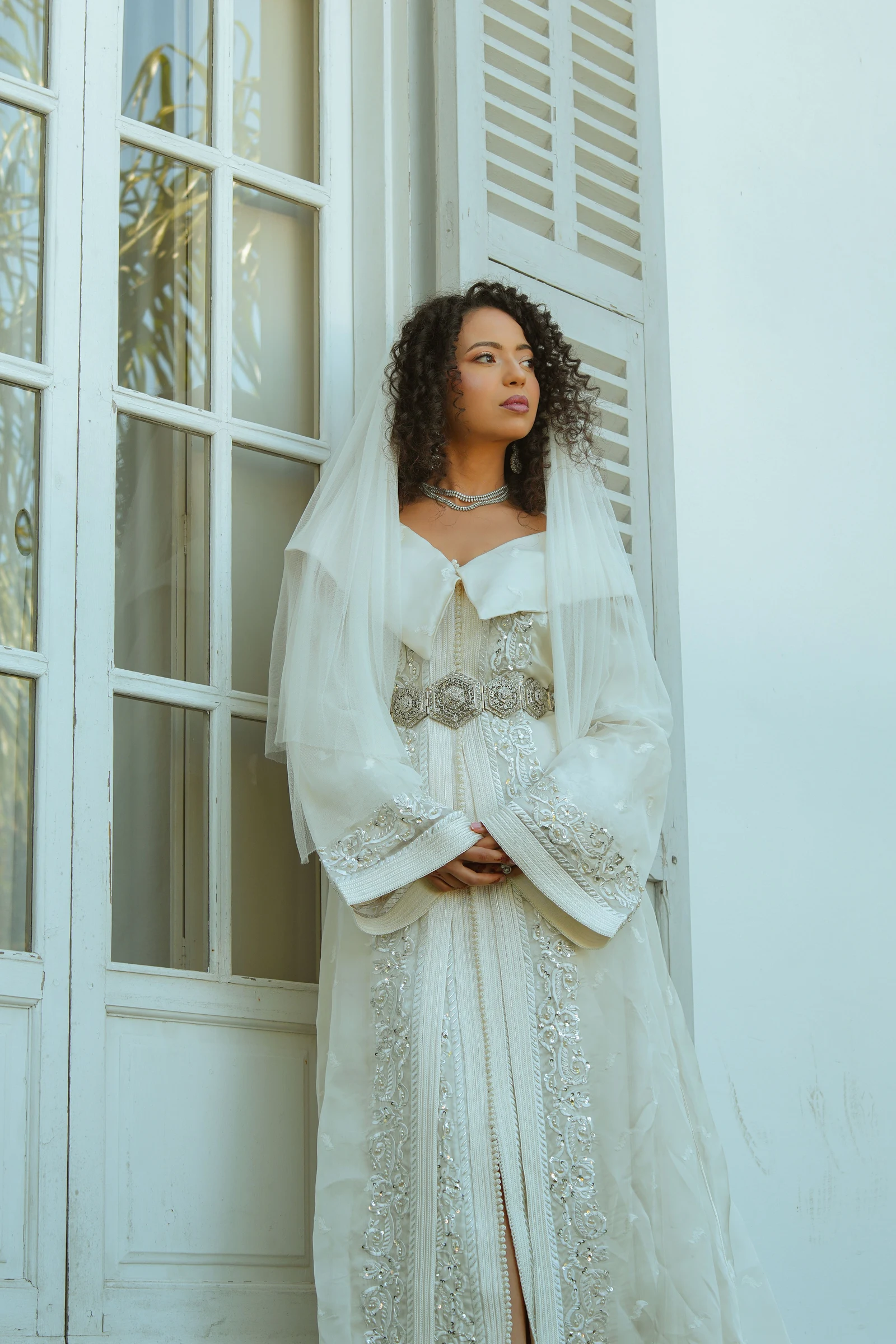 Femme en caftan blanc près d’une porte vitrée